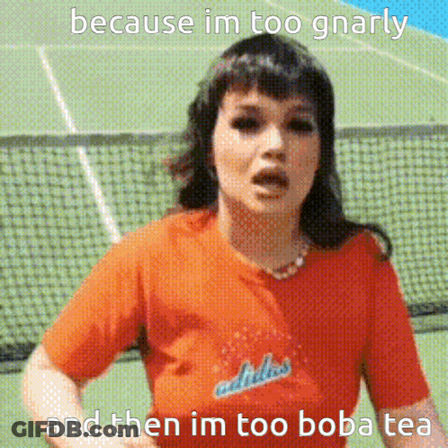 A Woman Wearing An Orange Adidas Shirt Is Standing In Front Of A Tennis Court GIF