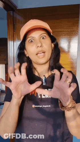 A Woman Wearing An Orange Hat Is Making A Funny Face With Her Hands GIF