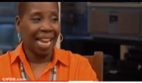 A Woman Wearing An Orange Shirt And Earrings Is Smiling . GIF