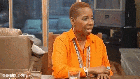 A Woman Wearing An Orange Shirt Is Sitting At A Table With A Glass Of Water . GIF
