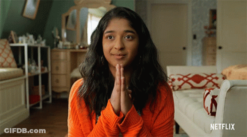 A Woman Wearing An Orange Sweater Is Praying With Her Hands Folded In Front Of Her Face .. GIF