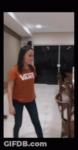 A Woman Wearing An Orange Vans Shirt Is Dancing In A Room GIF