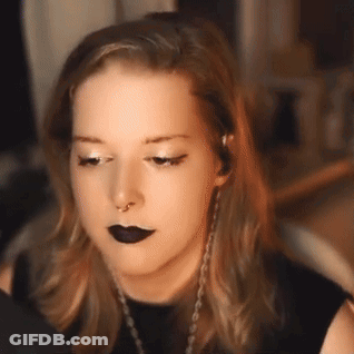 A Woman Wearing Black Lipstick And A Nose Ring Looks At The Camera . GIF