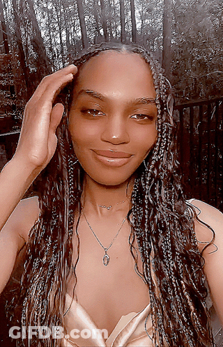 A Woman Wearing Braids And A Necklace Is Smiling For The Camera GIF