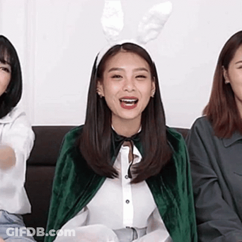 A Woman Wearing Bunny Ears And A Green Cape Is Sitting On A Couch With Two Other Women . GIF