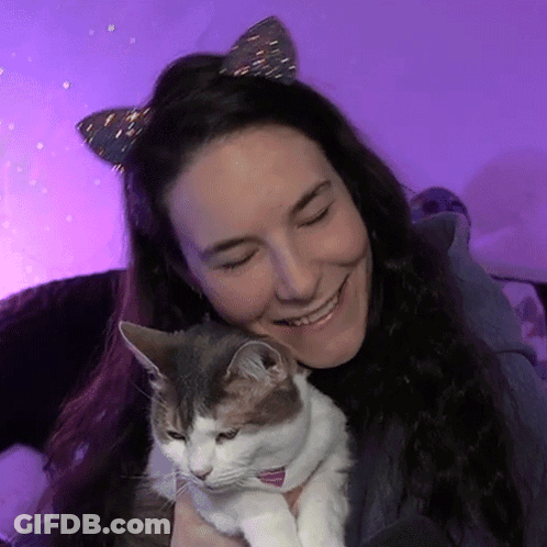 A Woman Wearing Cat Ears Is Holding A Cat In Her Arms GIF