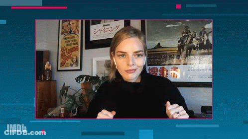 A Woman Wearing Ear Buds Stands In Front Of A Screen That Says Imdb On It GIF