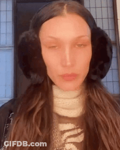 A Woman Wearing Ear Muffs And A Scarf Is Looking At The Camera . GIF