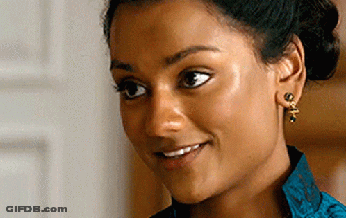 A Woman Wearing Earrings And A Blue Shirt Smiles GIF
