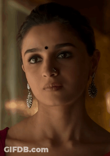 A Woman Wearing Earrings And A Nose Ring Has A Black Dot On Her Forehead GIF