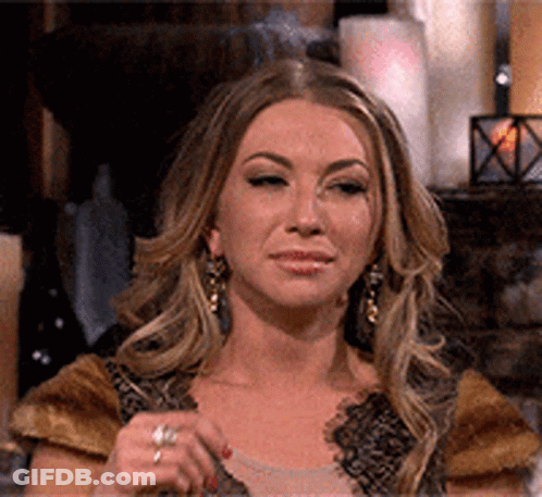 A Woman Wearing Earrings And A Ring Is Sitting In Front Of A Fireplace With Candles . GIF