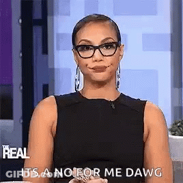 A Woman Wearing Glasses And A Black Dress Is Sitting On A Couch And Making A Face . GIF