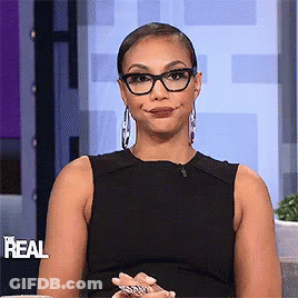 A Woman Wearing Glasses And A Black Dress Is Smiling And Making A Funny Face . GIF