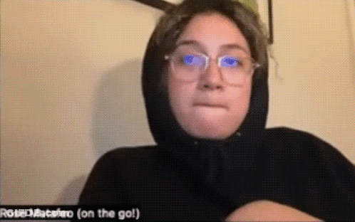 A Woman Wearing Glasses And A Black Hoodie Is Making A Face . GIF