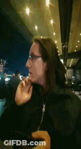 A Woman Wearing Glasses And A Black Jacket Looks At Her Phone GIF