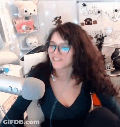 A Woman Wearing Glasses And A Black Shirt Is Sitting In Front Of A Microphone . GIF