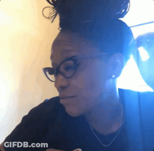 A Woman Wearing Glasses And A Black Shirt Looks Down At Something GIF