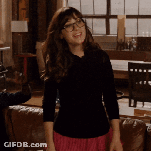 A Woman Wearing Glasses And A Black Shirt Stands In A Living Room GIF