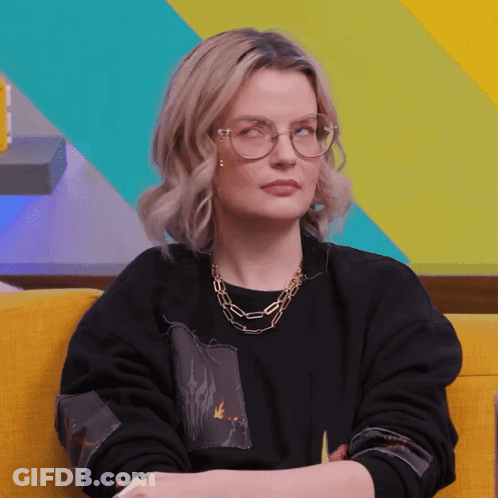 A Woman Wearing Glasses And A Black Sweater Is Sitting On A Yellow Couch GIF