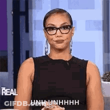A Woman Wearing Glasses And A Black Tank Top Is Sitting On A Couch And Smiling . GIF