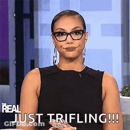A Woman Wearing Glasses And A Black Tank Top Is Sitting On A Couch And Smiling . GIF