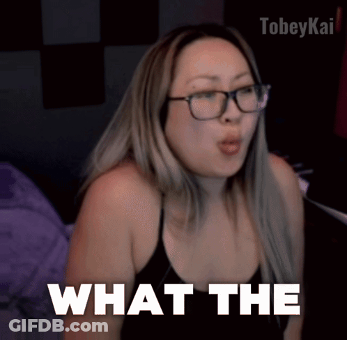 A Woman Wearing Glasses And A Black Top Says What The GIF