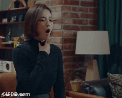 A Woman Wearing Glasses And A Black Turtleneck Is Yawning In A Living Room GIF