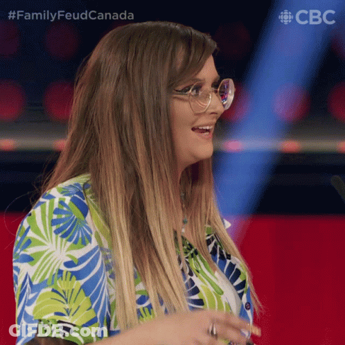 A Woman Wearing Glasses And A Blue And Green Shirt With The Words Family Feud Canada Behind Her GIF