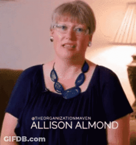A Woman Wearing Glasses And A Blue Necklace Has The Name Allison Almond On Her Shirt GIF