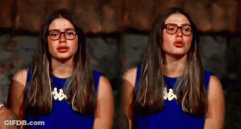 A Woman Wearing Glasses And A Blue Shirt Is Sitting In Front Of A Wall . GIF