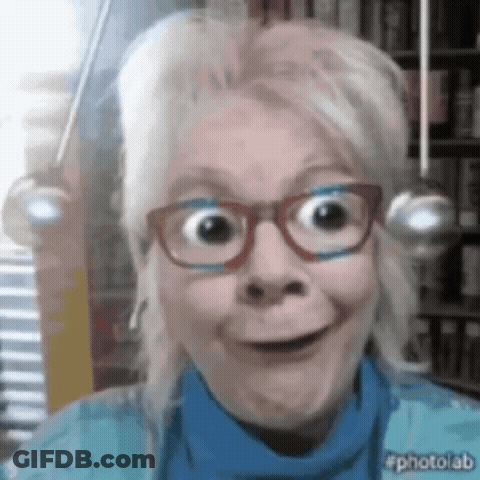 A Woman Wearing Glasses And A Blue Sweater Is Smiling For The Camera GIF