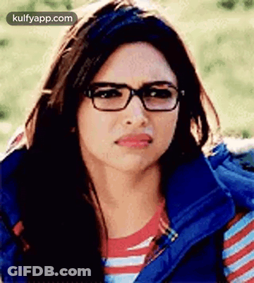 A Woman Wearing Glasses And A Blue Vest Is Making A Sad Face . GIF
