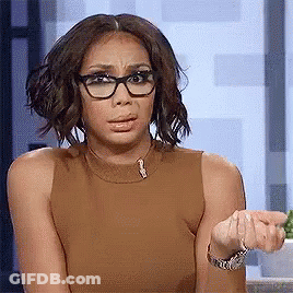A Woman Wearing Glasses And A Brown Tank Top Is Making A Face . GIF