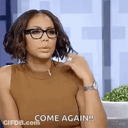 A Woman Wearing Glasses And A Brown Tank Top Is Sitting In Front Of A Wall And Says `` Come Again '' . GIF