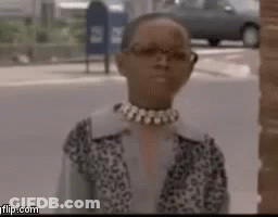 A Woman Wearing Glasses And A Choker Is Standing In Front Of A Brick Building . GIF
