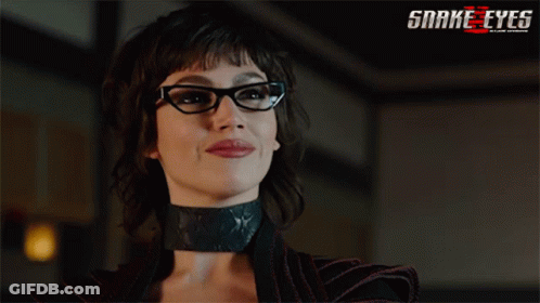 A Woman Wearing Glasses And A Choker With A Snake Eyes Logo Behind Her GIF