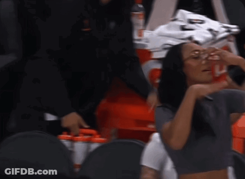 A Woman Wearing Glasses And A Crop Top Is Sitting In The Stands GIF