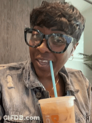 A Woman Wearing Glasses And A Denim Jacket Drinks Through A Straw From A Cup That Has The Letter D On It GIF