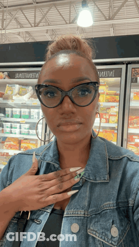 A Woman Wearing Glasses And A Denim Jacket Is Standing In Front Of A Fridge That Says ' Ii ' GIF