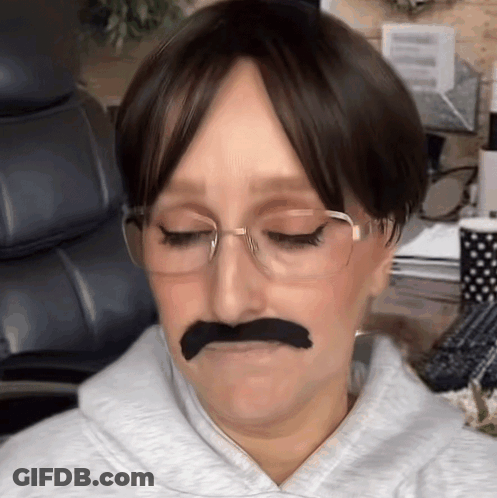 A Woman Wearing Glasses And A Fake Mustache Is Making A Funny Face GIF