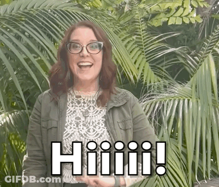 A Woman Wearing Glasses And A Green Jacket Is Standing In Front Of A Palm Tree And Smiling . GIF