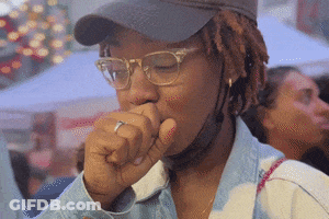 A Woman Wearing Glasses And A Hat Coughs GIF
