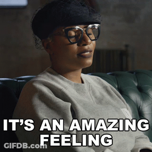 A Woman Wearing Glasses And A Hat Is Sitting On A Couch With The Words It 'S An Amazing Feeling Above Her GIF
