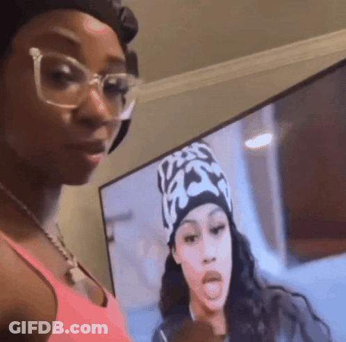 A Woman Wearing Glasses And A Hat Is Standing In Front Of A Television Screen . GIF