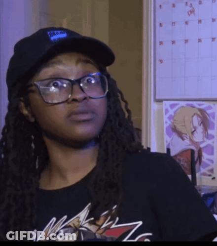 A Woman Wearing Glasses And A Hat With The Letter T On It Is Standing In Front Of A Calendar GIF