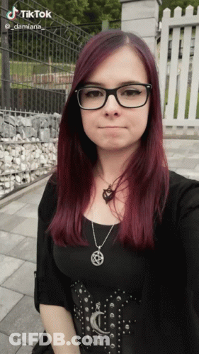 A Woman Wearing Glasses And A Necklace With A Pentagram On It Takes A Selfie GIF
