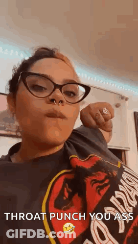 A Woman Wearing Glasses And A Nose Ring Is Giving A Throat Punch To The Camera . GIF
