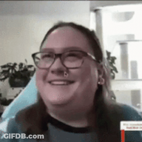 A Woman Wearing Glasses And A Nose Ring Is Smiling . GIF