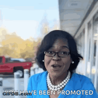 A Woman Wearing Glasses And A Pearl Necklace Is Talking To Someone . GIF