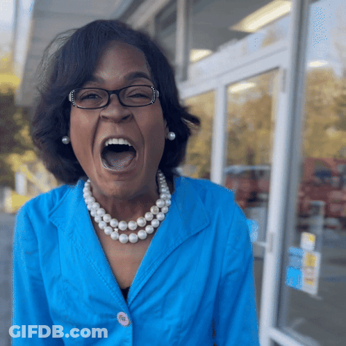 A Woman Wearing Glasses And A Pearl Necklace Screams With Her Mouth Open GIF